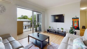 Una sala de estar moderna con un sofá, una mesa de centro, un televisor y un ventanal corredero que da a un balcón.