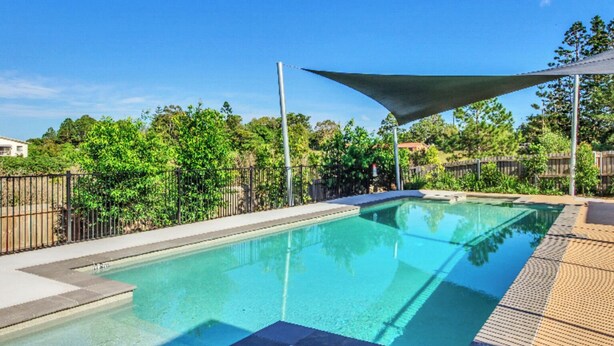 Una piscina cristalina con zona sombreada, rodeada por una valla y vegetación.