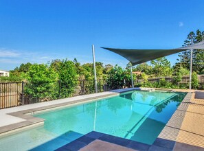A clear swimming pool with a shaded area, surrounded by a fence and greenery. - Homely Townhouse with Pools (Moreton Bay City)