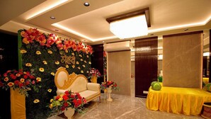 A reception area with a sofa, a table with a yellow tablecloth, and a wall decorated with flowers and a sign. - Evara By Meraki Inn (Kolkata)