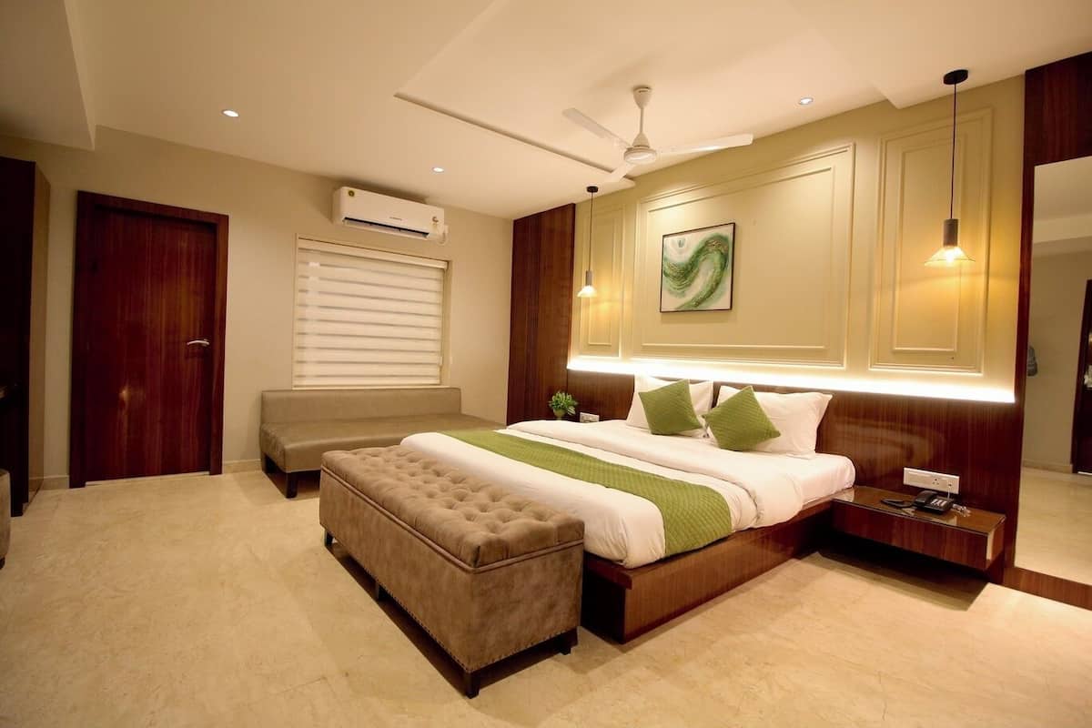 A modern bedroom with a large bed, a bedside table, a nightstand, a bench, an air conditioning unit, and a ceiling fan.