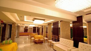 A spacious, well-lit banquet hall with a round table and chairs, a sofa, and a decorative chandelier. - Evara By Meraki Inn (Kolkata)
