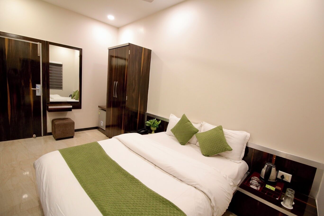 Ein Hotelzimmer mit Bett, Schrank, Spiegel und Nachttisch mit Wasserkocher.
