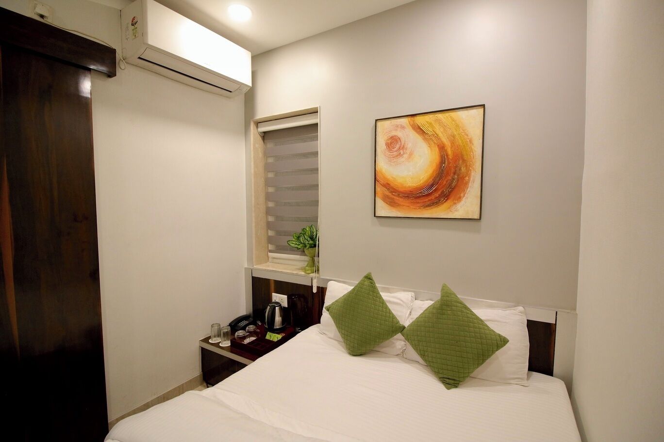 A hotel room with a bed, a nightstand, a small window, and a wall-mounted air conditioner.