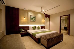 A modern bedroom with a large bed, a bedside table with a lamp, a ceiling fan, and a view of a bathroom. - Evara By Meraki Inn (Kolkata)