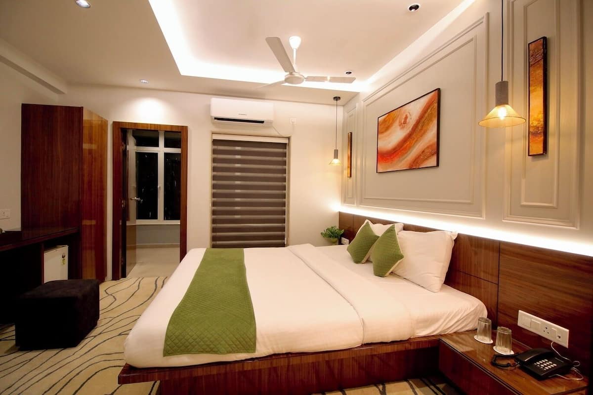 A hotel room with a large bed, a desk, a chair, a ceiling fan, and a window with blinds.
