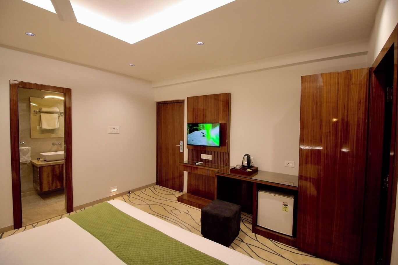 Una habitación de hotel moderna con una cama grande, televisión, una kitchenette pequeña y un espejo.