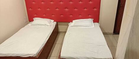 Deux lits simples avec du linge de lit blanc et une tête de lit rouge à motifs capitonnés dans une petite pièce.