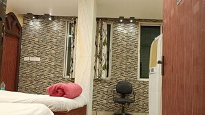Une chambre à coucher comprenant un lit, une chaise, une fenêtre et un mur dont le motif rappelle celui de la pierre.