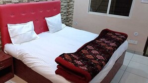 Une chambre avec une tête de lit rouge, une table de chevet en bois, une couverture à motifs et un mur imitant la pierre.