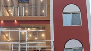 Un hôtel à plusieurs étages, avec une façade rouge, des balcons dotés de rampes et une voiture garée devant.