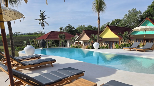 A poolside area with lounge chairs and umbrellas, surrounded by palm trees and a clear sky. - UNITED COLORS OF BALI NATURE (Tibubeneng)