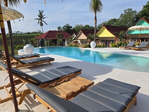 A poolside area with lounge chairs and umbrellas, surrounded by palm trees and a clear sky. - UNITED COLORS OF BALI NATURE (Tibubeneng)