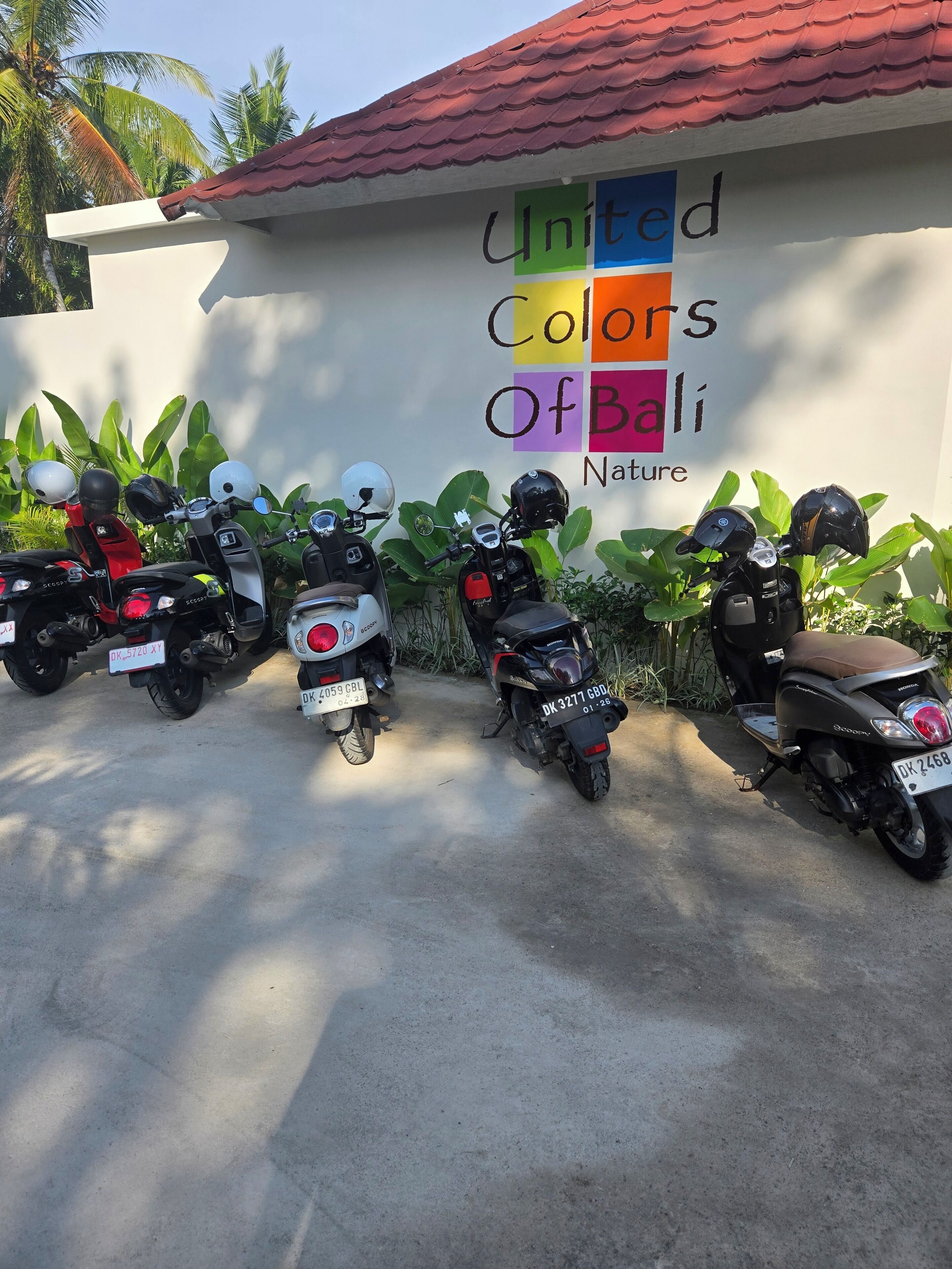 Una fila de scooters estacionados frente a un edificio con un cartel que dice 'United Colors of Bali Nature'.