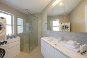 A modern bathroom with a glass-enclosed shower, a washing machine, and a large mirror.