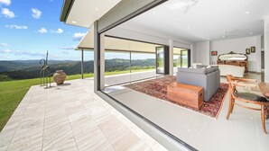 Ein modernes Interieur mit einer großen Glasdoor, die auf einen Balkon führt, ein graues Sofa, eine Holzablage und ein Esstisch mit Stühlen.