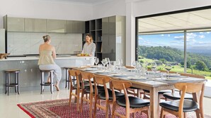 Eine moderne Küche mit einer großen Kochinsel, einem Essbereich mit Holzkästen und Blick auf eine grüne Landschaft durch große Fenster.