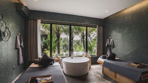 A modern spa room with a large round bathtub, two massage tables, and a view of palm trees through large windows. - Maar Resort Ubud by Ini Vie Hospitality (Payangan)
