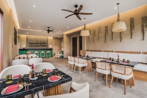 A modern dining area with multiple tables, chairs, ceiling fans, and decorative wall art. - Maar Resort Ubud by Ini Vie Hospitality (Payangan)