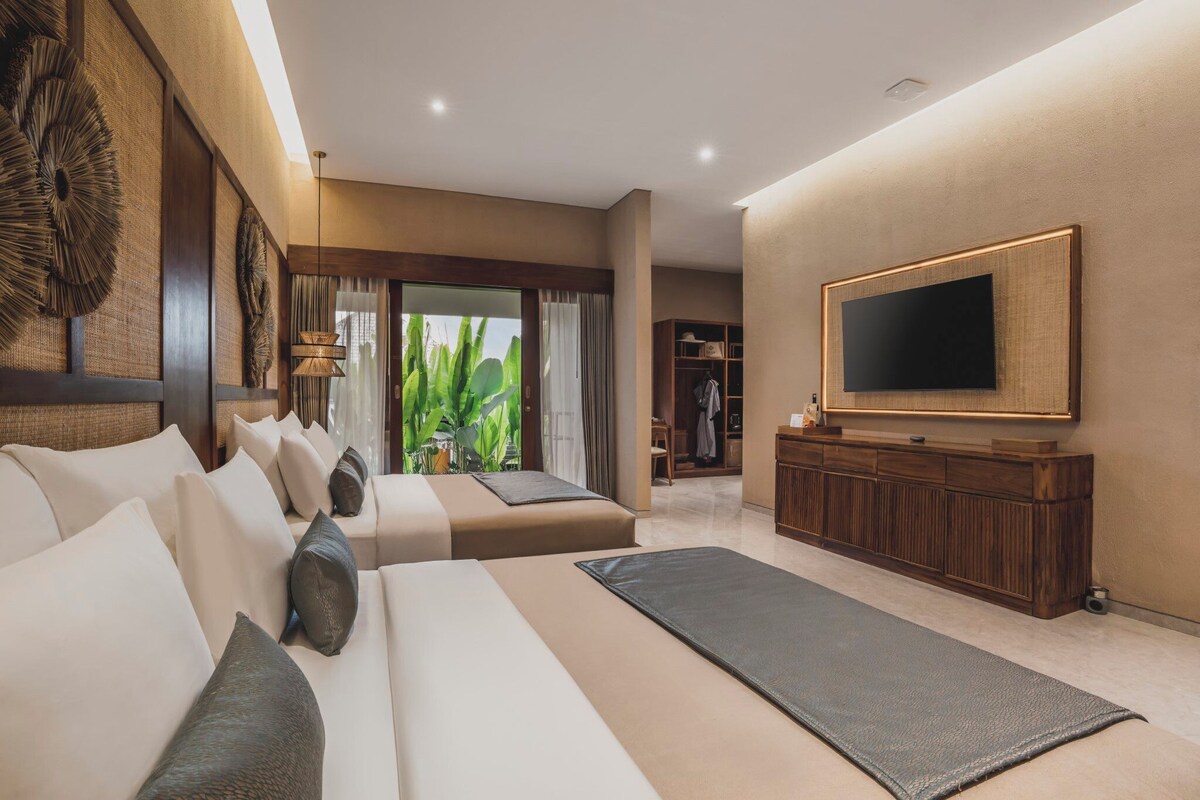 A modern hotel room with a large bed, a TV, a seating area, and a view of greenery.