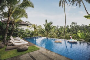 Una piscina con sillas de descanso y una plataforma flotante, rodeada de vegetación tropical.