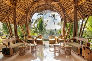 Una habitación con techo de paja, muebles de bambú y vistas a palmeras.