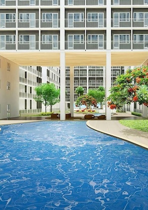 A modern building with a swimming pool, surrounded by greenery and a covered walkway.
