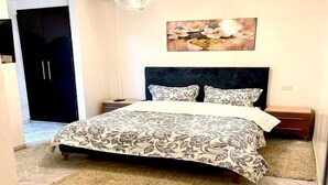 A bedroom with a bed, a nightstand, a wall-mounted painting, and a door. - Cozy 1BR Retreat, Steps to Sand (Sousse)