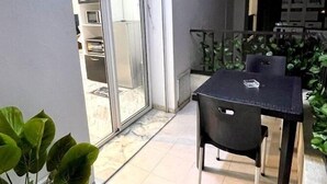 A patio area with a table and chairs, a sliding glass door leading to a kitchen, and potted plants. - Cozy 1BR Retreat, Steps to Sand (Sousse)