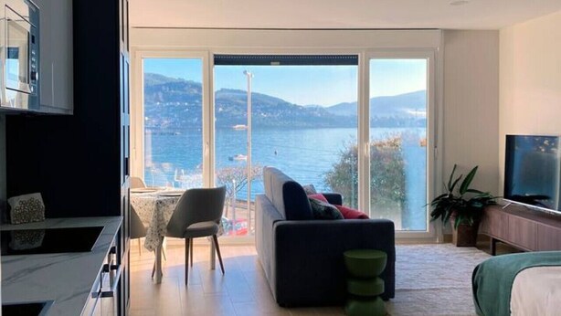 A modern living room with a large window, a sofa, a dining area, and a TV.