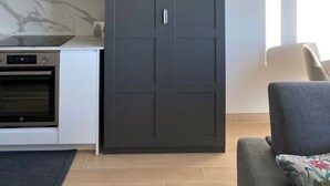A modern kitchen with white cabinets, a dark grey wardrobe, and a grey sofa.