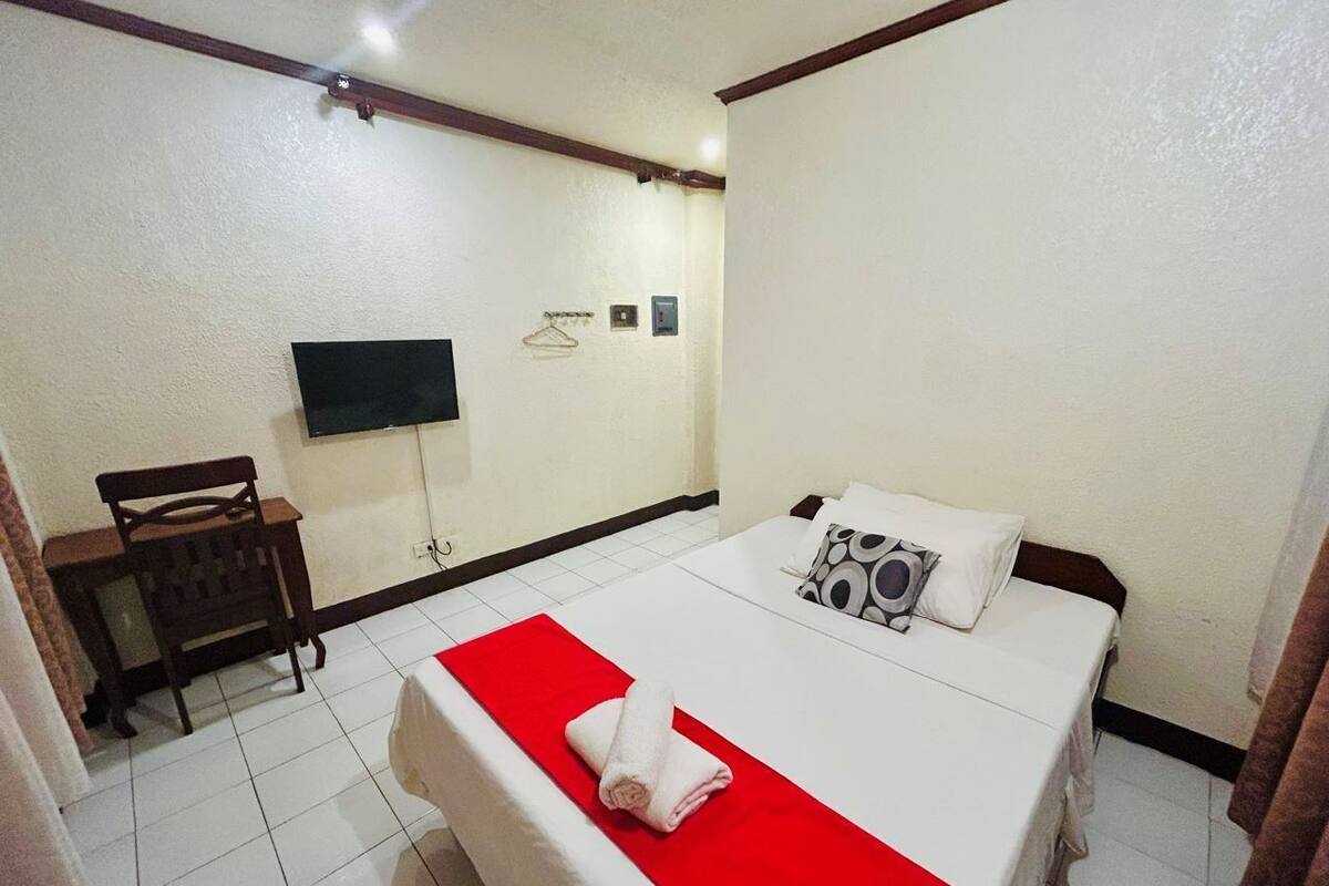 A hotel room with a bed, a TV mounted on the wall, a chair, and a small desk.