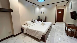 A hotel room with a bed, bedside table, and a small wooden stool.