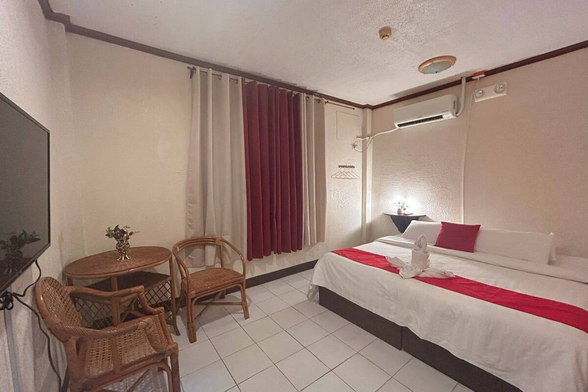 A hotel room with a bed, a bedside table, a chair, a small round table, and a TV.