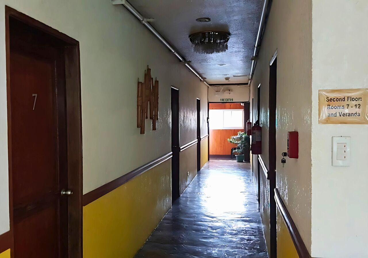 Un pasillo con un letrero de salida de incendios, un extintor y un cartel que indica las habitaciones 7-12 y Veranda en el segundo piso.