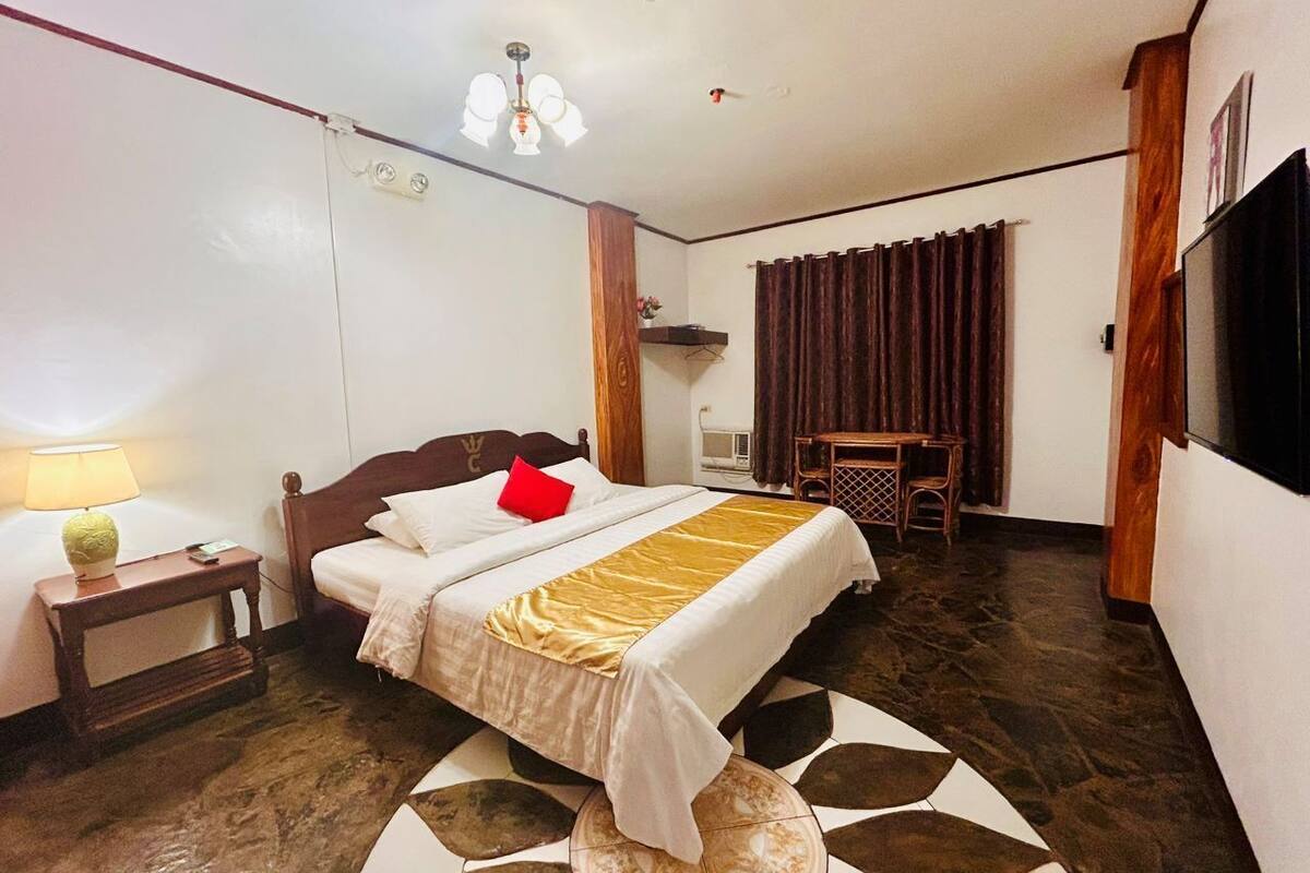A hotel room with a bed, bedside table, lamp, and a television.
