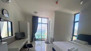 A hotel room with a bed, a desk, a chair, a TV, and a view of the sea.
