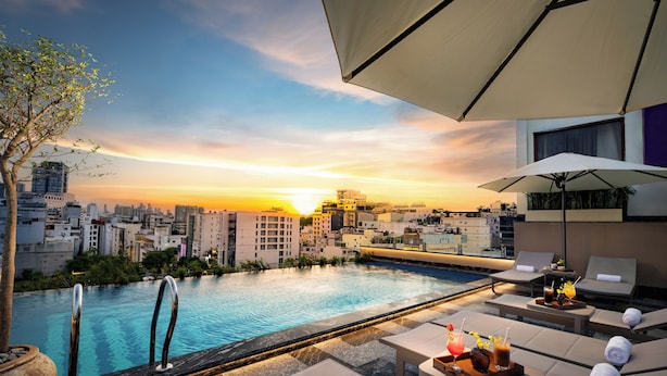 A rooftop pool area with lounge chairs and umbrellas, overlooking a cityscape at sunset. - GRAND HOTEL du LAC Boutique Saigon (Ho Chi Minh City)