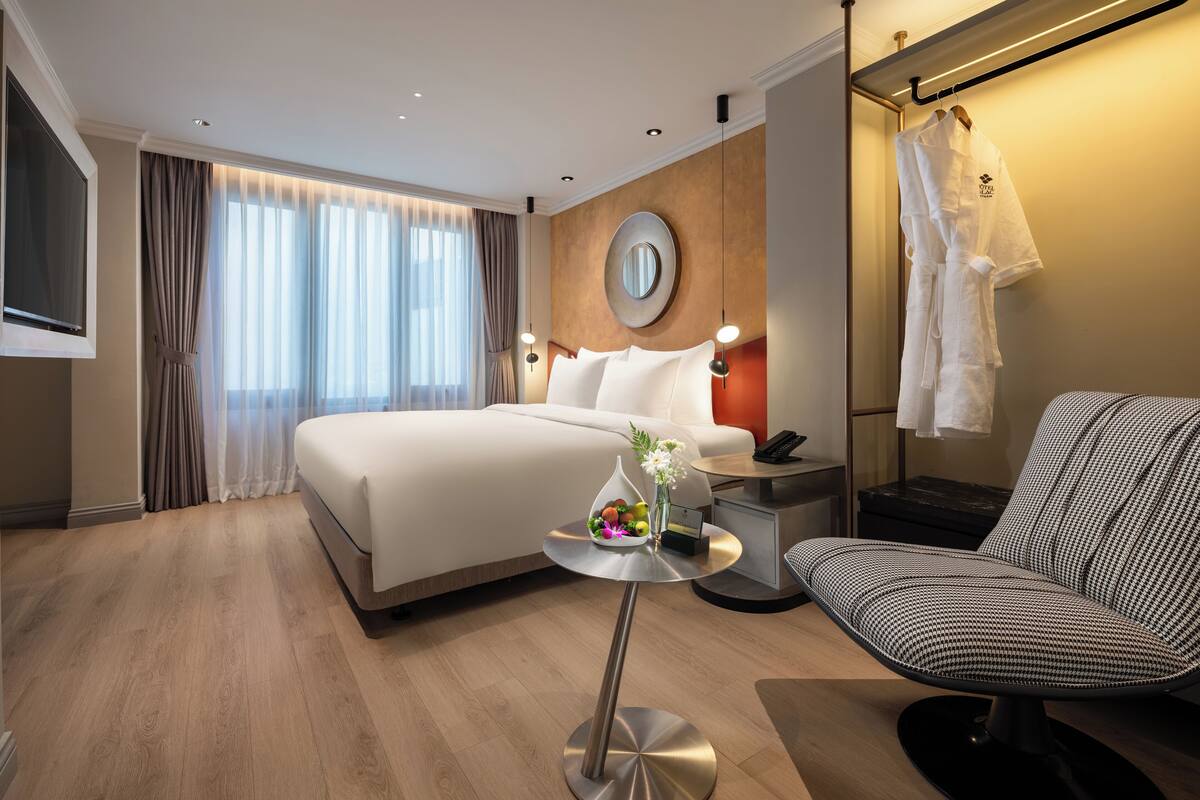 A modern hotel room with a large bed, bedside table, chair, and a TV.