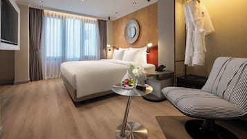 A modern hotel room with a large bed, bedside table, chair, and a TV.