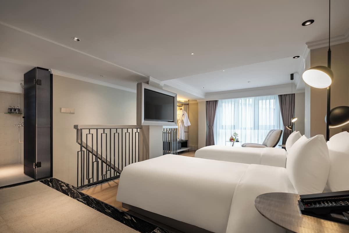 A hotel room with two beds, a TV, a desk, and a balcony.