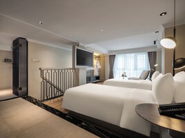 Ein Hotelzimmer mit zwei Betten, einem Fernseher, einem Schreibtisch und einem Balkon.