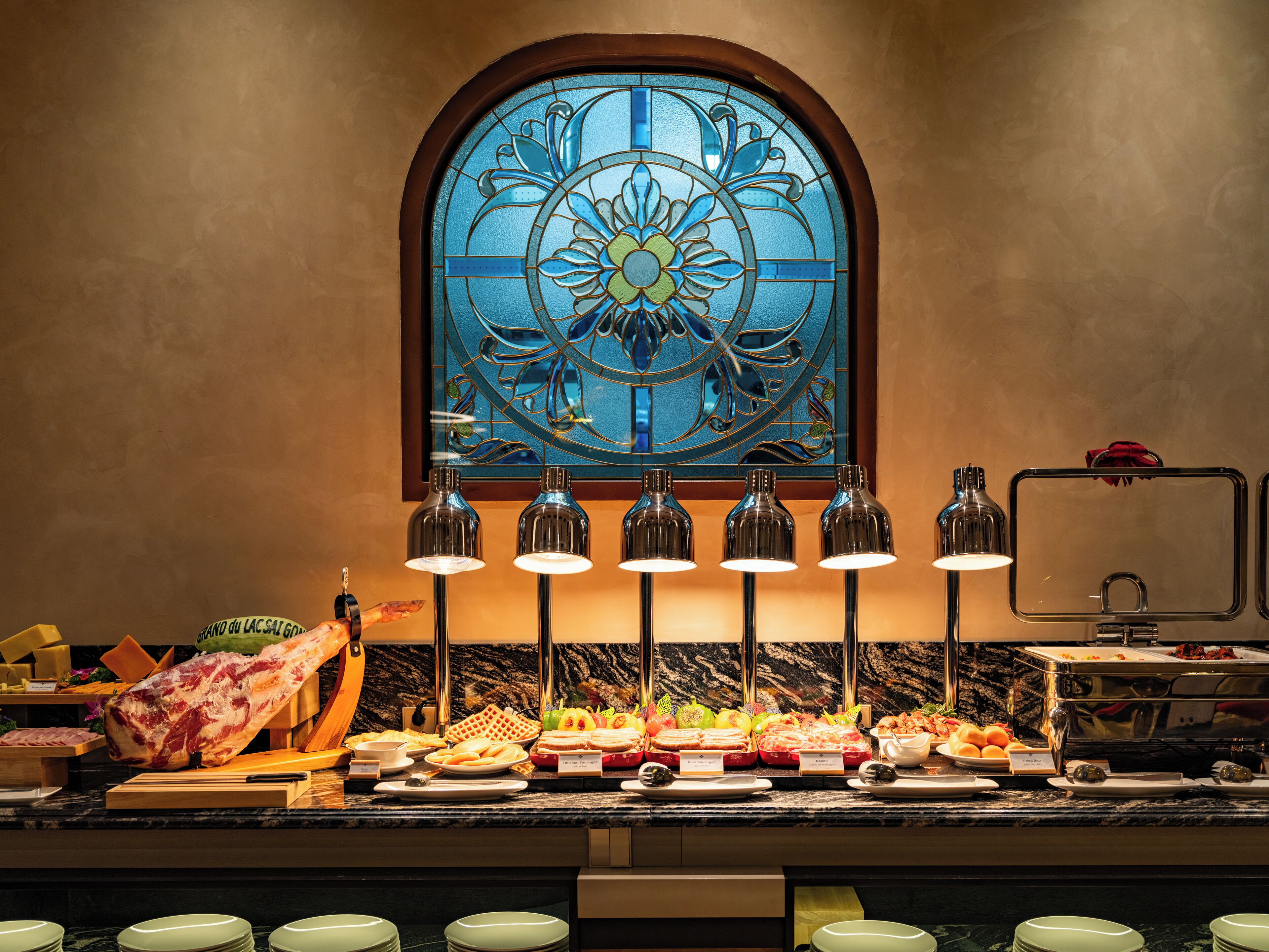 A buffet with various food items, a large meat centerpiece, and a stained glass window in the background.