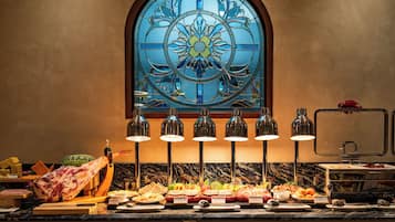 Un bufé con diversas opciones de comida, una gran pieza central de carne y una ventana de vitral al fondo.