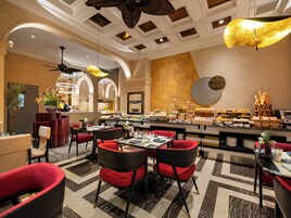 Um saguão de hotel com buffet, cadeiras vermelhas, piso de mármore e uma grande parede decorativa.