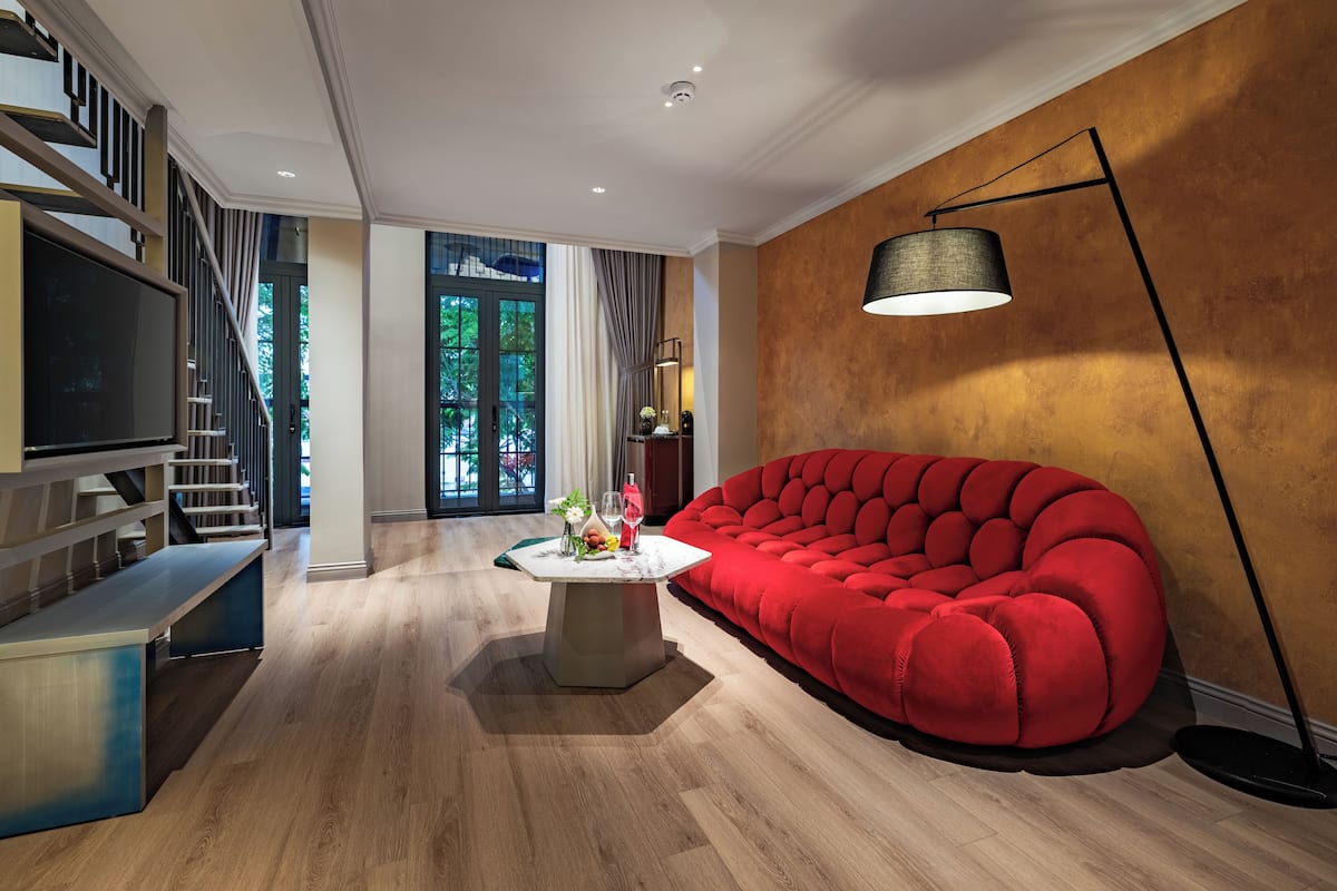 A modern living room with a red sofa, a coffee table, and a TV. There is a staircase with a railing and a door leading outside.