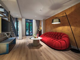A modern living room with a red sofa, a coffee table, and a TV. There is a staircase with a railing and a door leading outside.