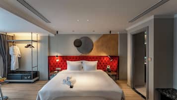 A modern hotel room with a large bed, a red headboard, a bedside table with a lamp, and a wardrobe with a mirror.