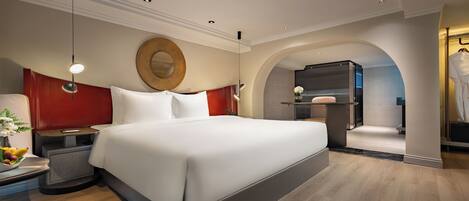 A modern hotel room with a large bed, a round mirror, a vanity, and a view of the bathroom.