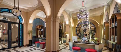A spacious lobby with a large clock, red and blue seating, and a central reception desk.